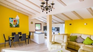 A modern living room with a dining area, a kitchen in the background, and a yellow wall.