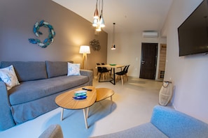 A modern living room with a grey sofa, a wooden coffee table, and a dining area with a table and chairs.