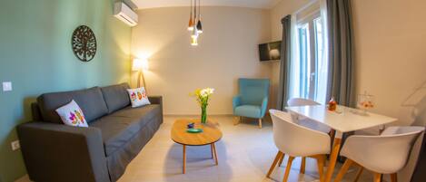A modern living room with a sofa, a coffee table, a dining table with chairs, a TV, and a window with curtains.