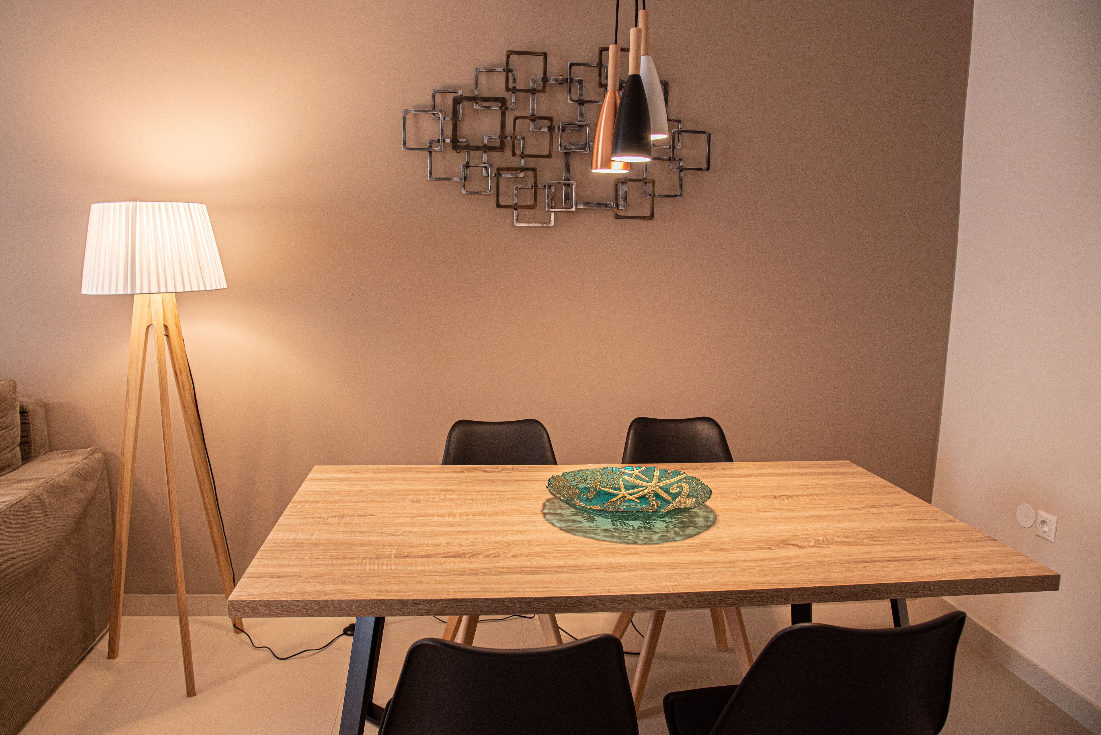 Un coin repas comprenant une table en bois, deux chaises, un bol décoratif, une lampe et une œuvre d’art géométrique accrochée au mur.