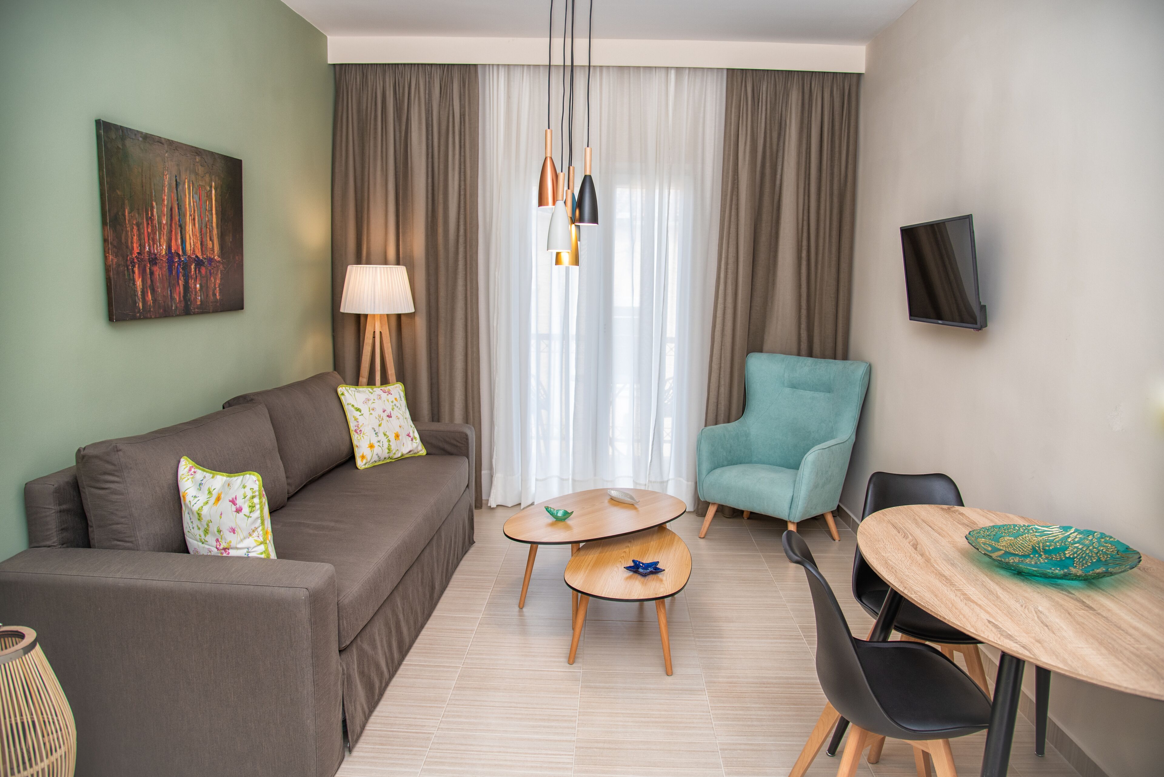 A modern living room with a sofa, a teal armchair, a small round table, and a TV mounted on the wall.