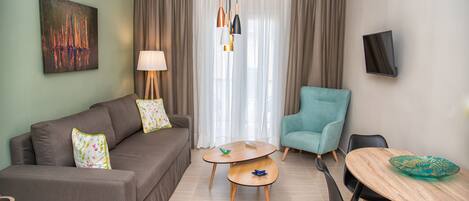 A modern living room with a sofa, a teal armchair, a small round table, and a TV mounted on the wall.