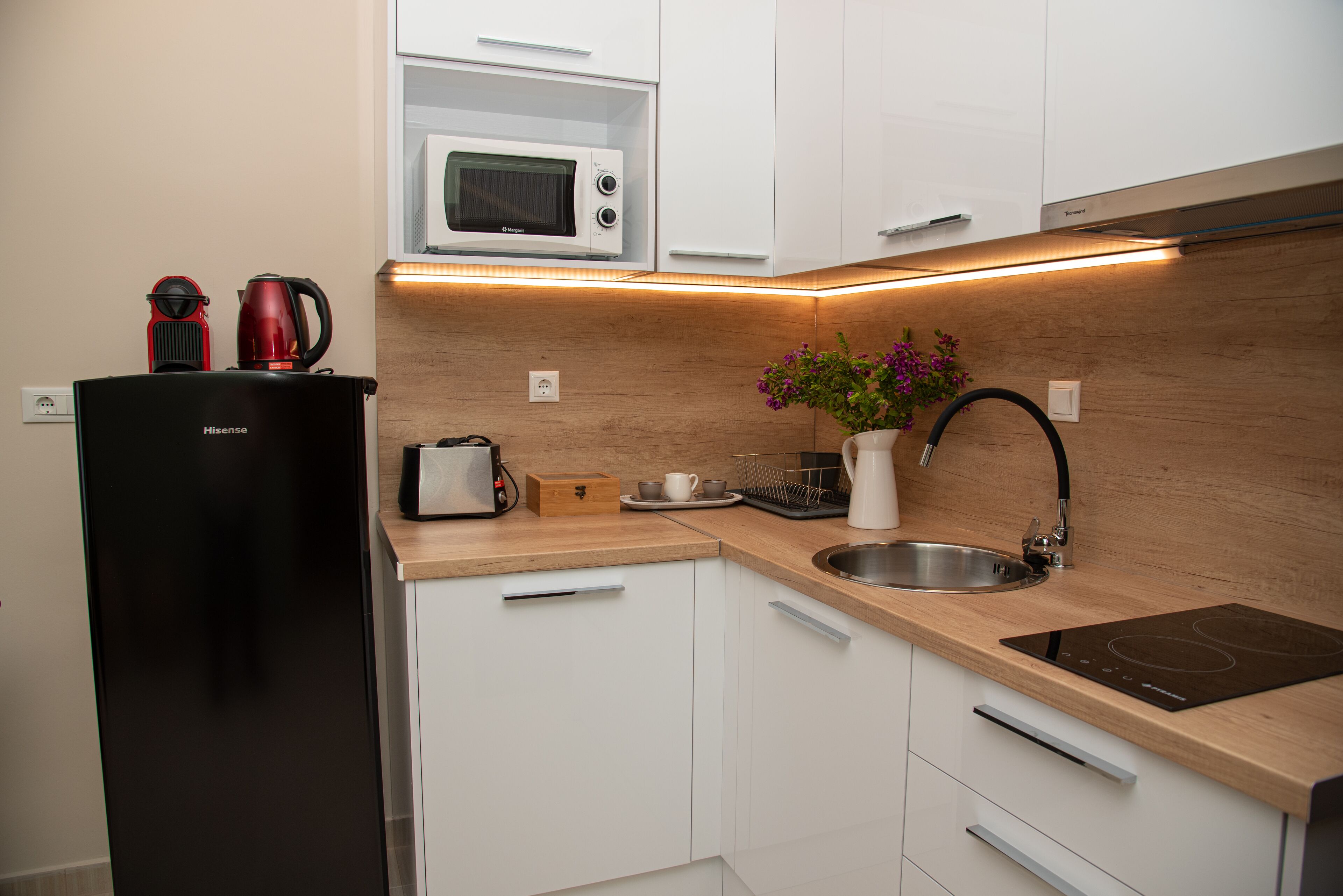 A compact kitchen with white cabinets, a black refrigerator, a microwave, a sink, and an induction cooktop.