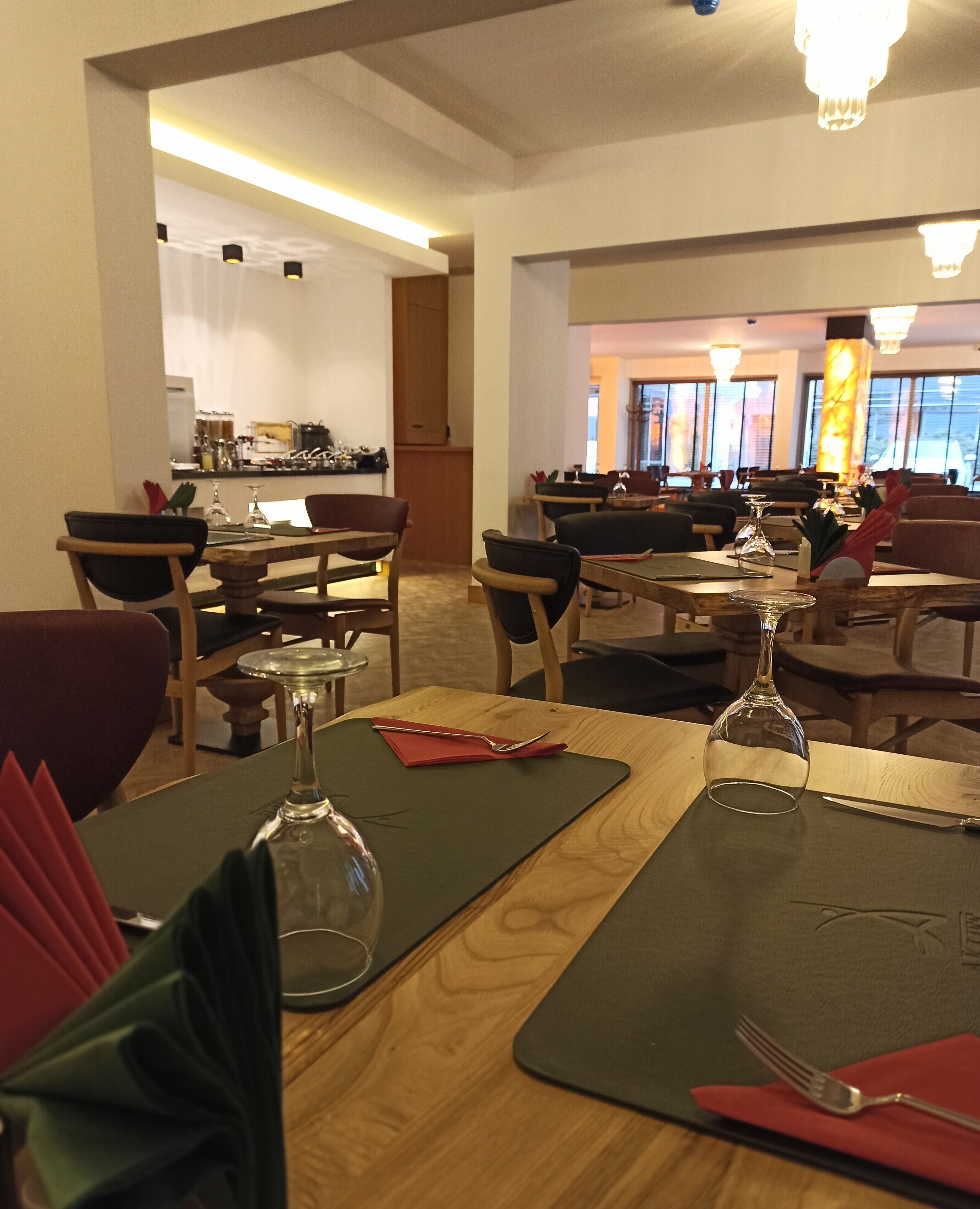 Un restaurante con mesas y sillas de madera, una zona de bar y vistas a la ciudad a través de amplios ventanales.
