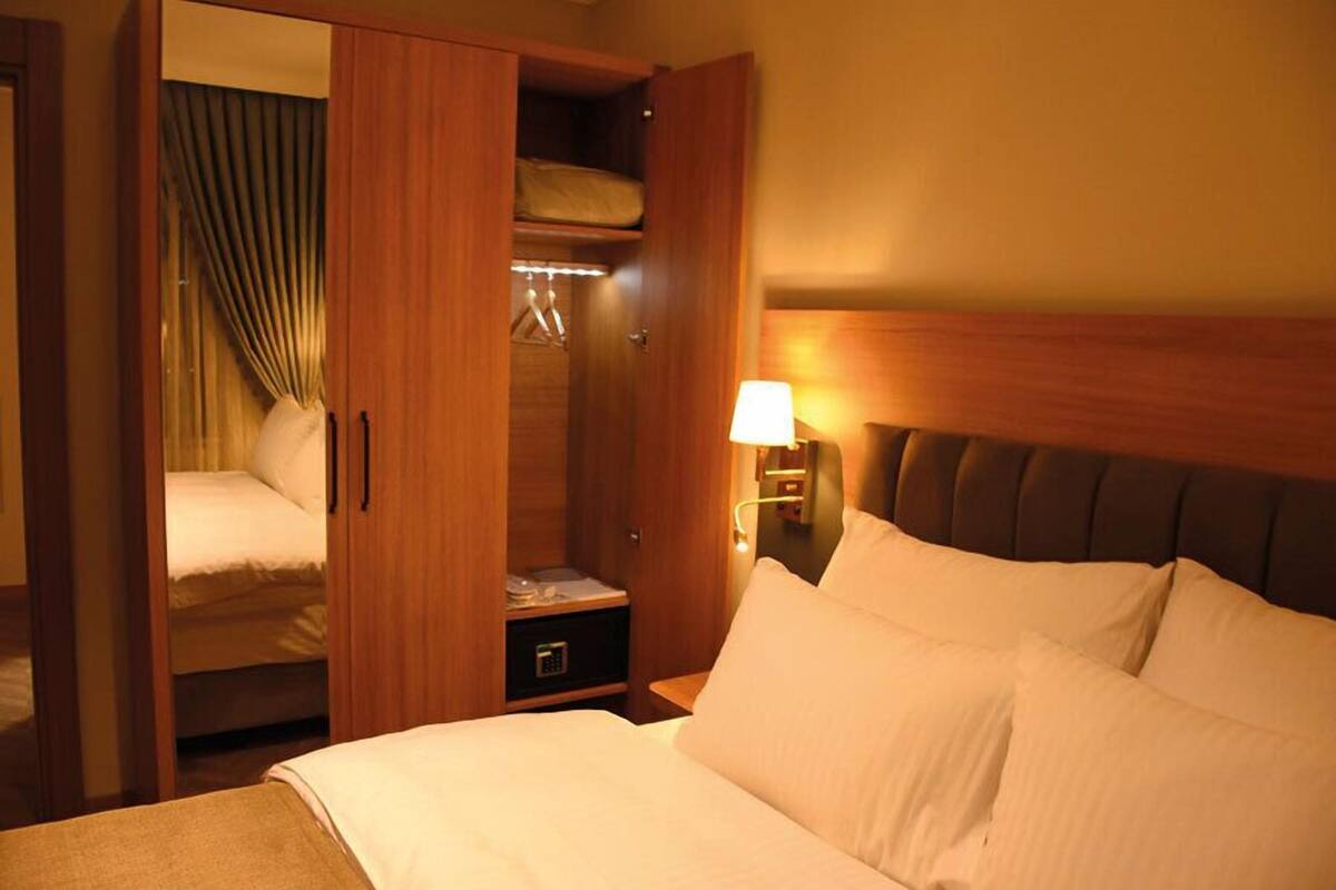 Una habitación de hotel con una cama, un armario y una mesita de noche con lámpara.