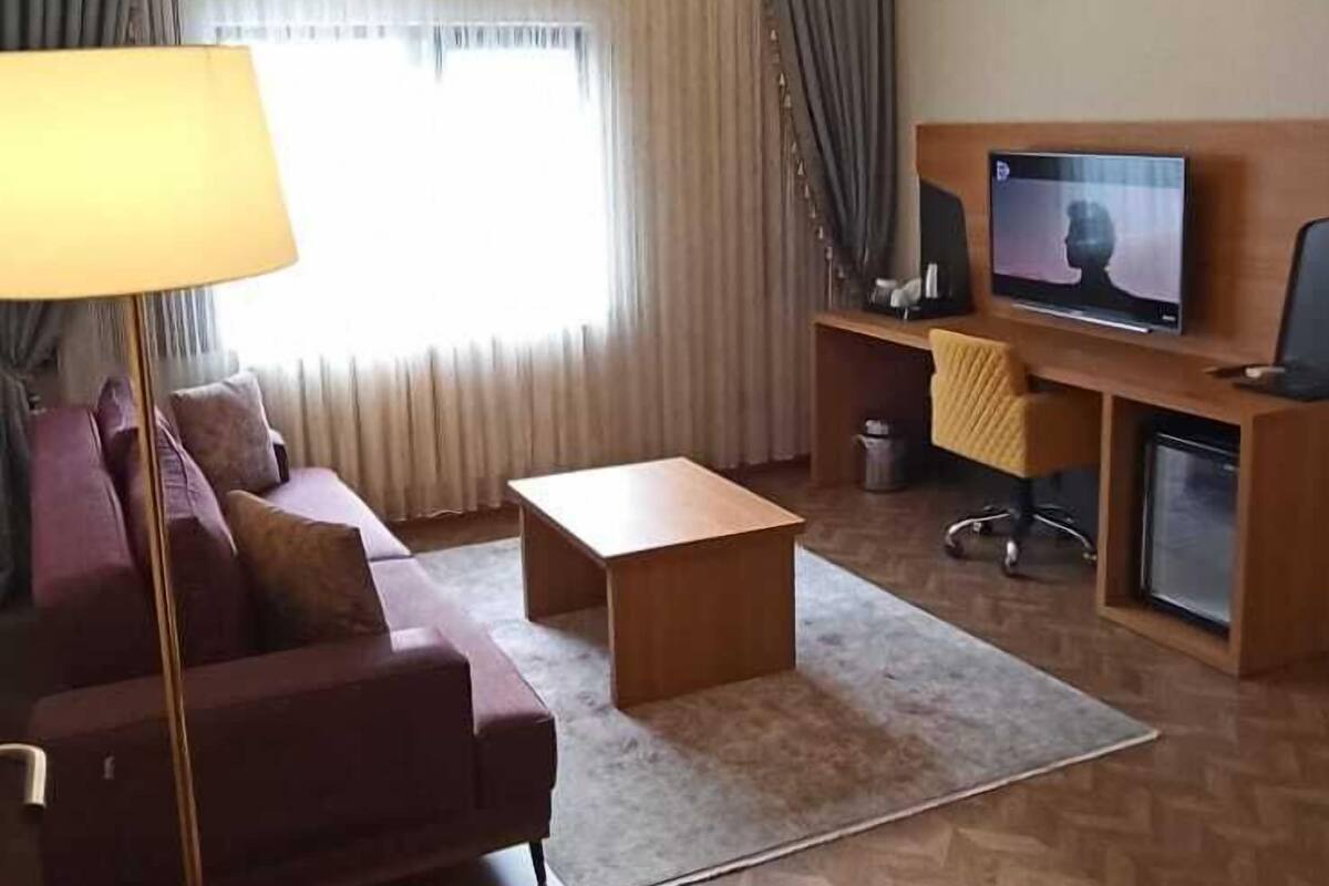 Habitación de hotel con sofá, mesa de centro, televisor y escritorio con computadora.