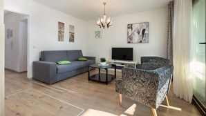 A modern living room with a grey sofa, patterned armchair, and a flat-screen TV on a white stand. - Newly renovated Apartment with WiFi and BBQ (Pula)