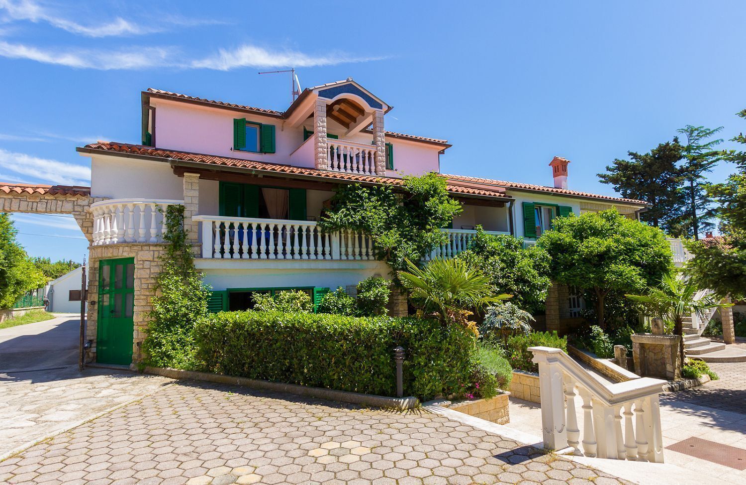 A two-story house with a balcony, a stone entrance, and a paved driveway.