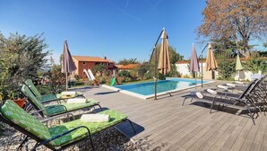 Un área junto a la piscina con sillones de descanso, sombrillas y un cielo azul despejado.