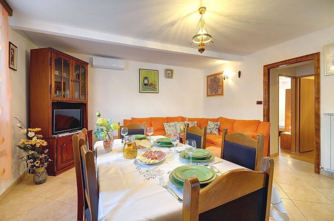 Un coin repas avec une table dressée pour quatre personnes, un téléviseur et un canapé en arrière-plan.