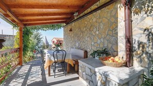 Un patio al aire libre con pared de piedra, pérgola de madera, una mesa con sillas y una cesta de fruta.
