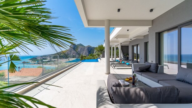 A modern balcony with a view of the sea and mountains, a sofa, and a pool area. - Luxurious Villa ADA with hot tub, sauna, gym, infinity pool, sea views! (Omiš)