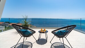 A balcony with two black wire-framed chairs, a small round table with a plate of food, and a potted plant. - Luxurious Villa ADA with hot tub, sauna, gym, infinity pool, sea views! (Omiš)