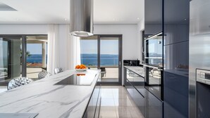 A modern kitchen with a large island, stainless steel appliances, and a view of the sea. - Luxurious Villa ADA with hot tub, sauna, gym, infinity pool, sea views! (Omiš)