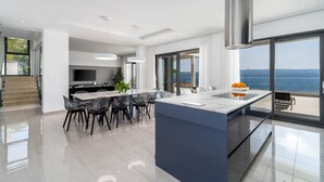A modern kitchen with a large island, a dining area with chairs, and a view of the sea. - Luxurious Villa ADA with hot tub, sauna, gym, infinity pool, sea views! (Omiš)
