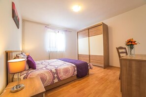 A bedroom with a bed, bedside table, lamp, window with curtains, wardrobe, and a desk with a vase of flowers. - Air-conditioned flat with jacuzzi, sun loungers, Wi-Fi (Maruzini)