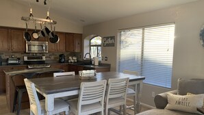 A modern kitchen with wooden cabinets, stainless steel appliances, and a dining area with white chairs. - *** GORGEOUS DESERT GETAWAY WITH HEATED  POOL NEAR THE DUKE GOLF COURSE*** (Maricopa)
