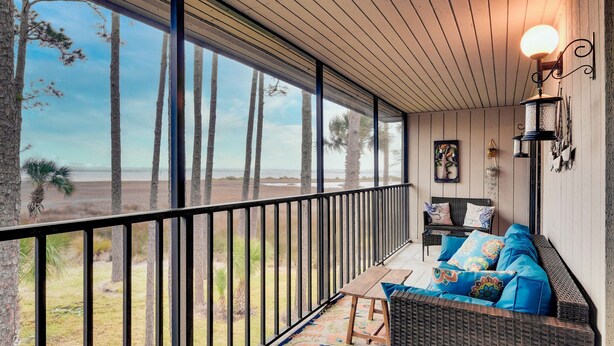 Un balcón con vista a la playa, muebles de mimbre y una lámpara de pared.