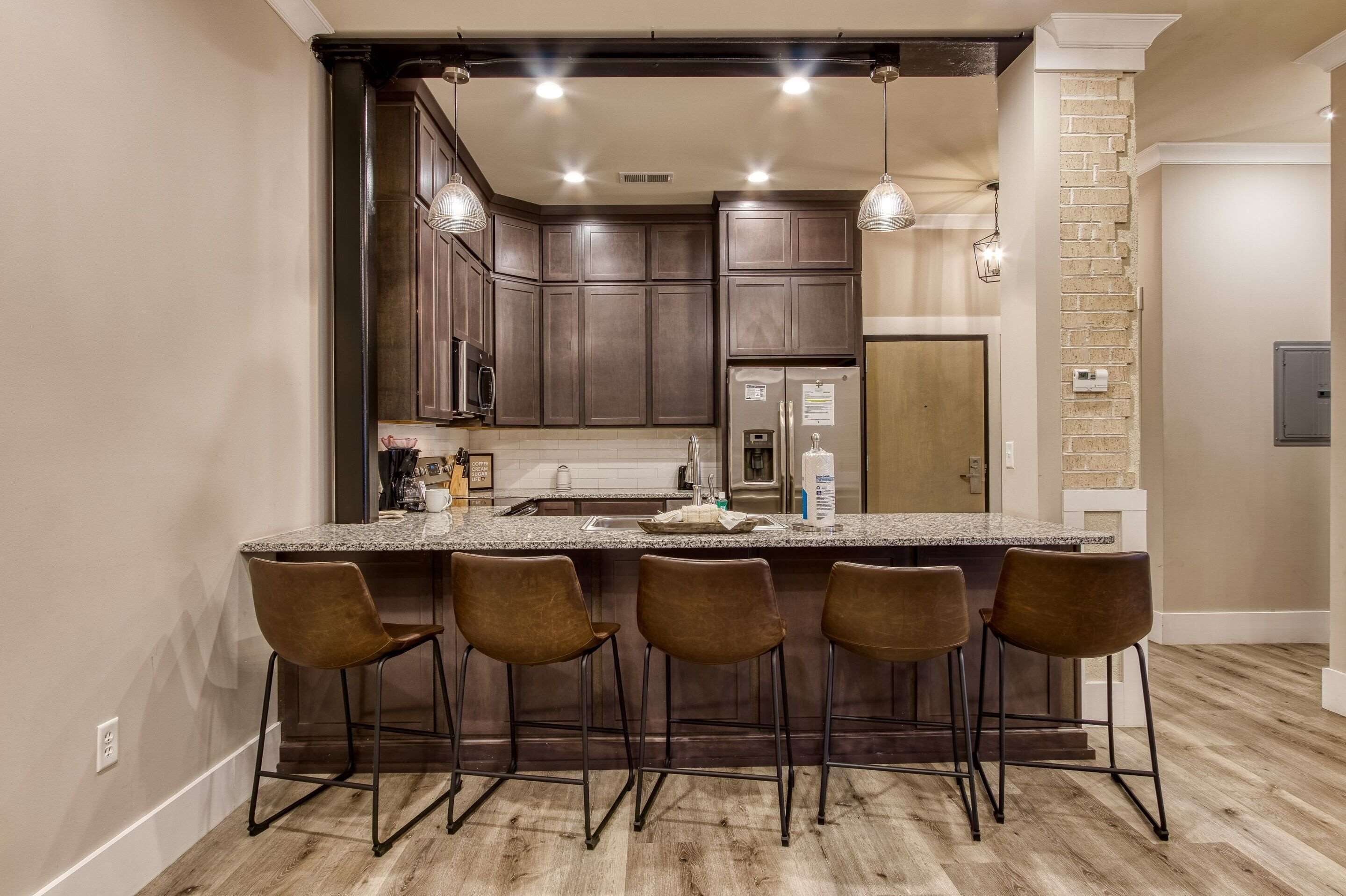 A kitchen with a central island, dark wooden cabinets, and bar stools.