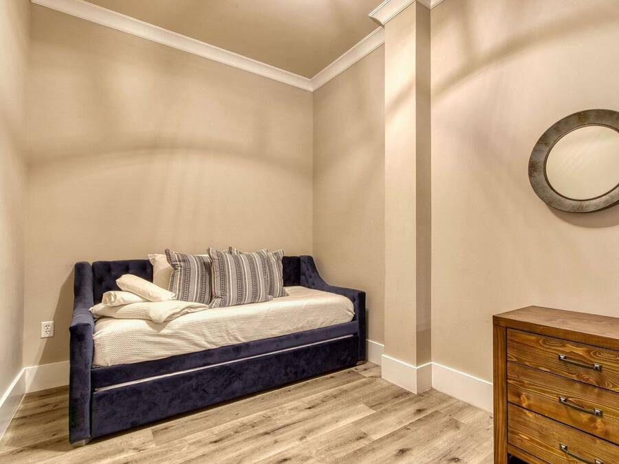 A bedroom with a dark blue bed, a wooden dresser, and a round mirror on the wall.