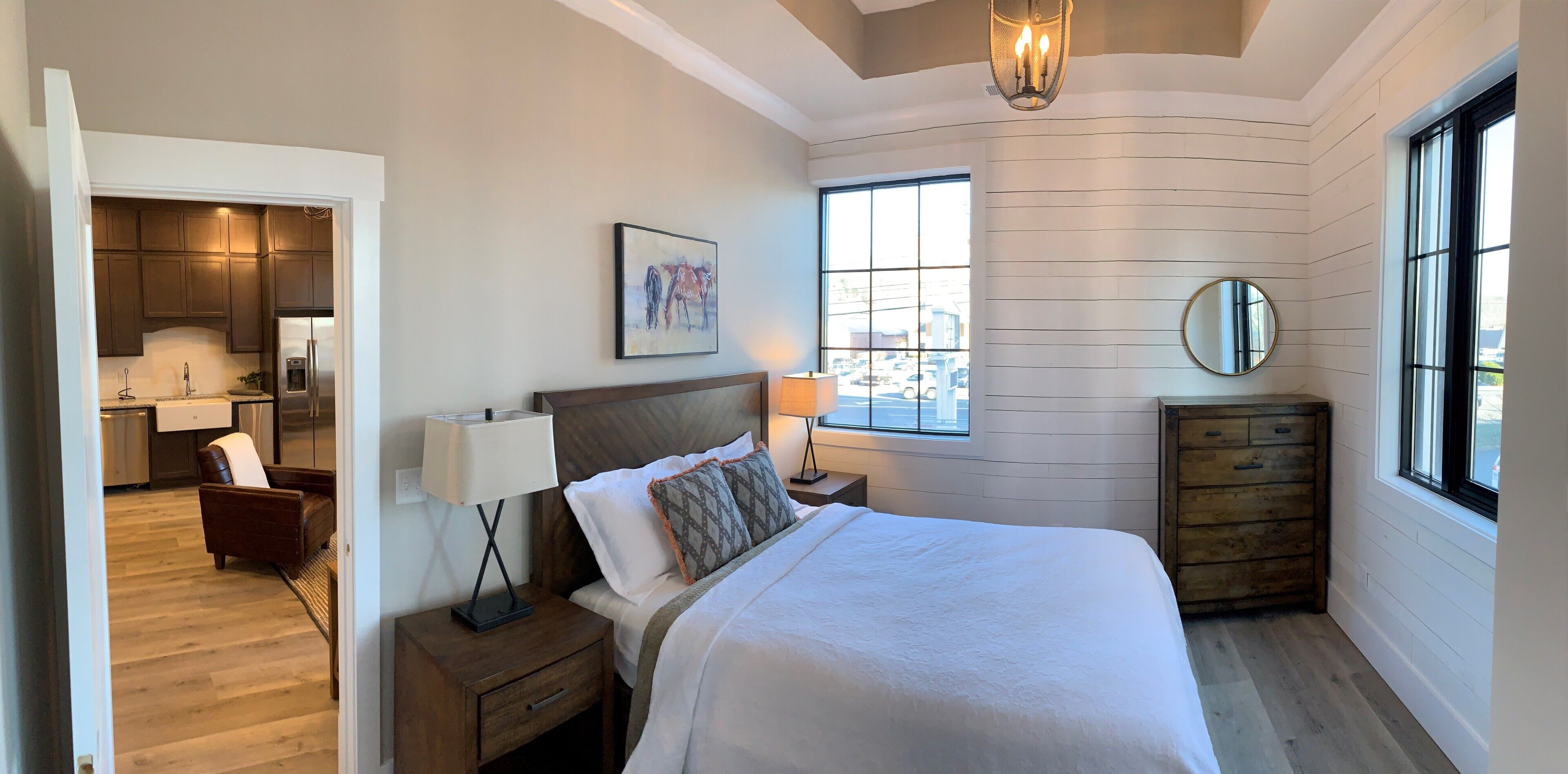 A bedroom with a bed, bedside table, lamp, dresser, and a window with a view.