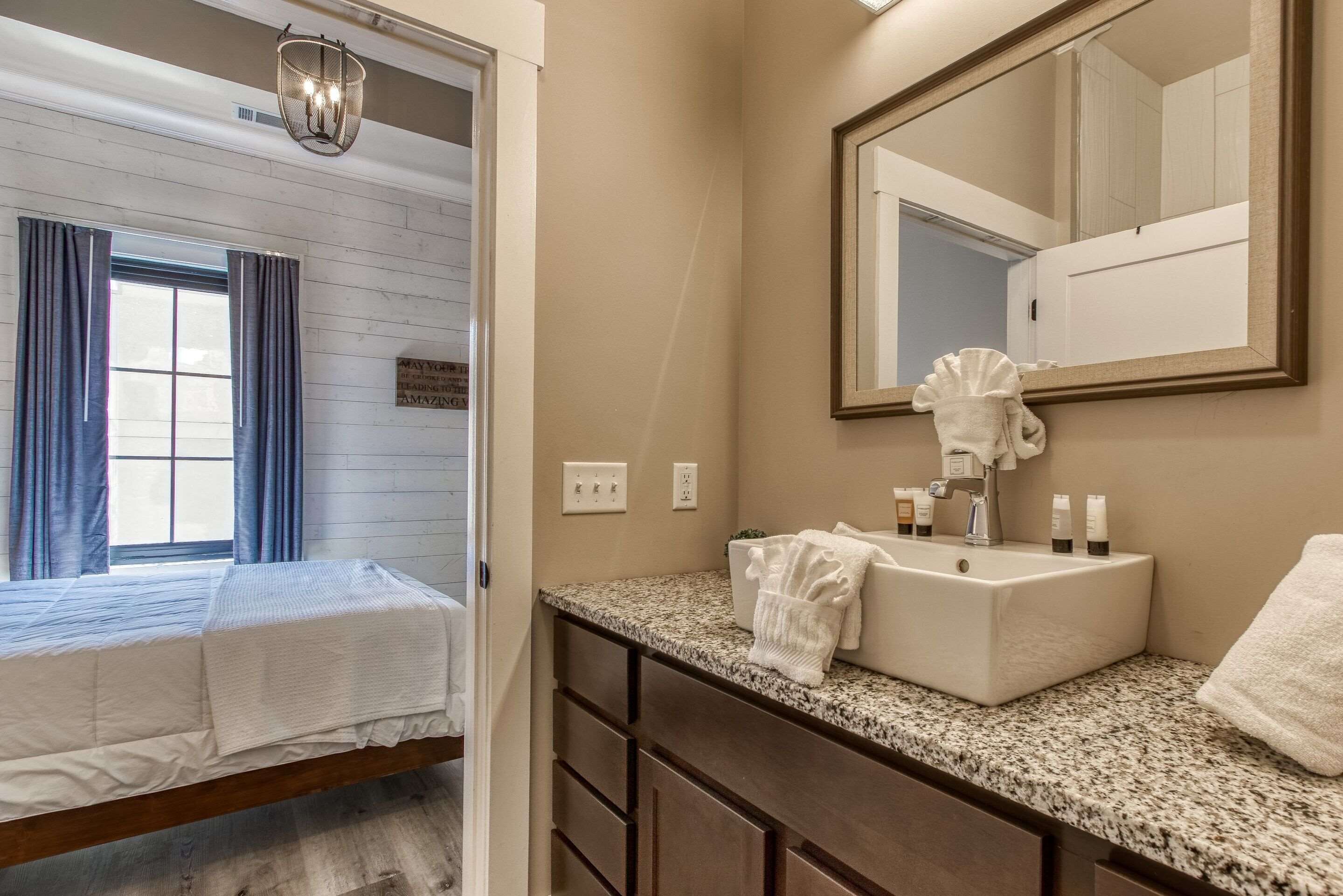 A hotel room with a bed, a bathroom with a sink, mirror, and toiletries.