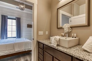 A hotel room with a bed, a bathroom with a sink, mirror, and toiletries. - The Historic Central Hotel, a New Hotel Collection Property (Sevierville)