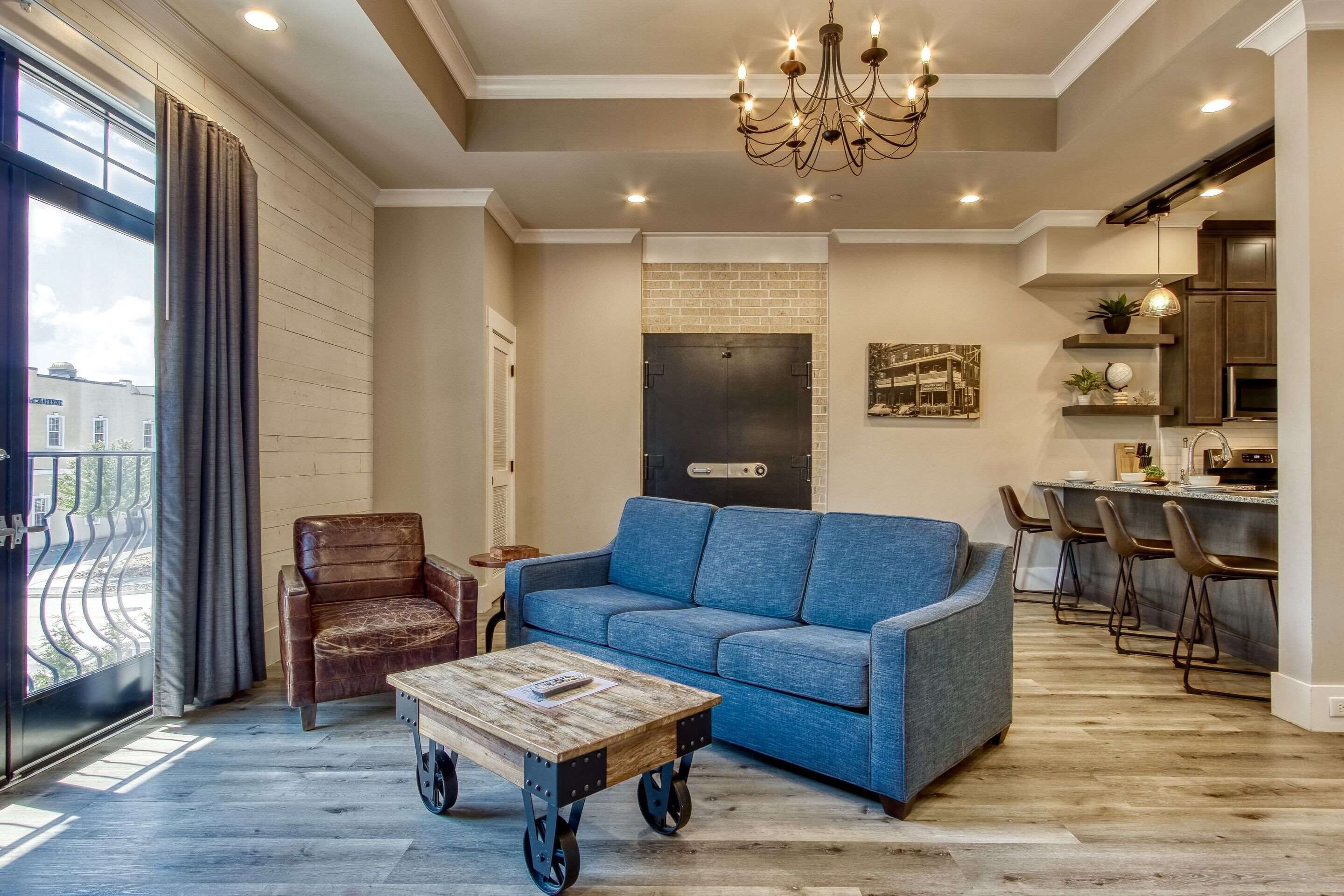 A spacious living area with a blue sofa, a brown leather chair, and a wooden coffee table with wheels.