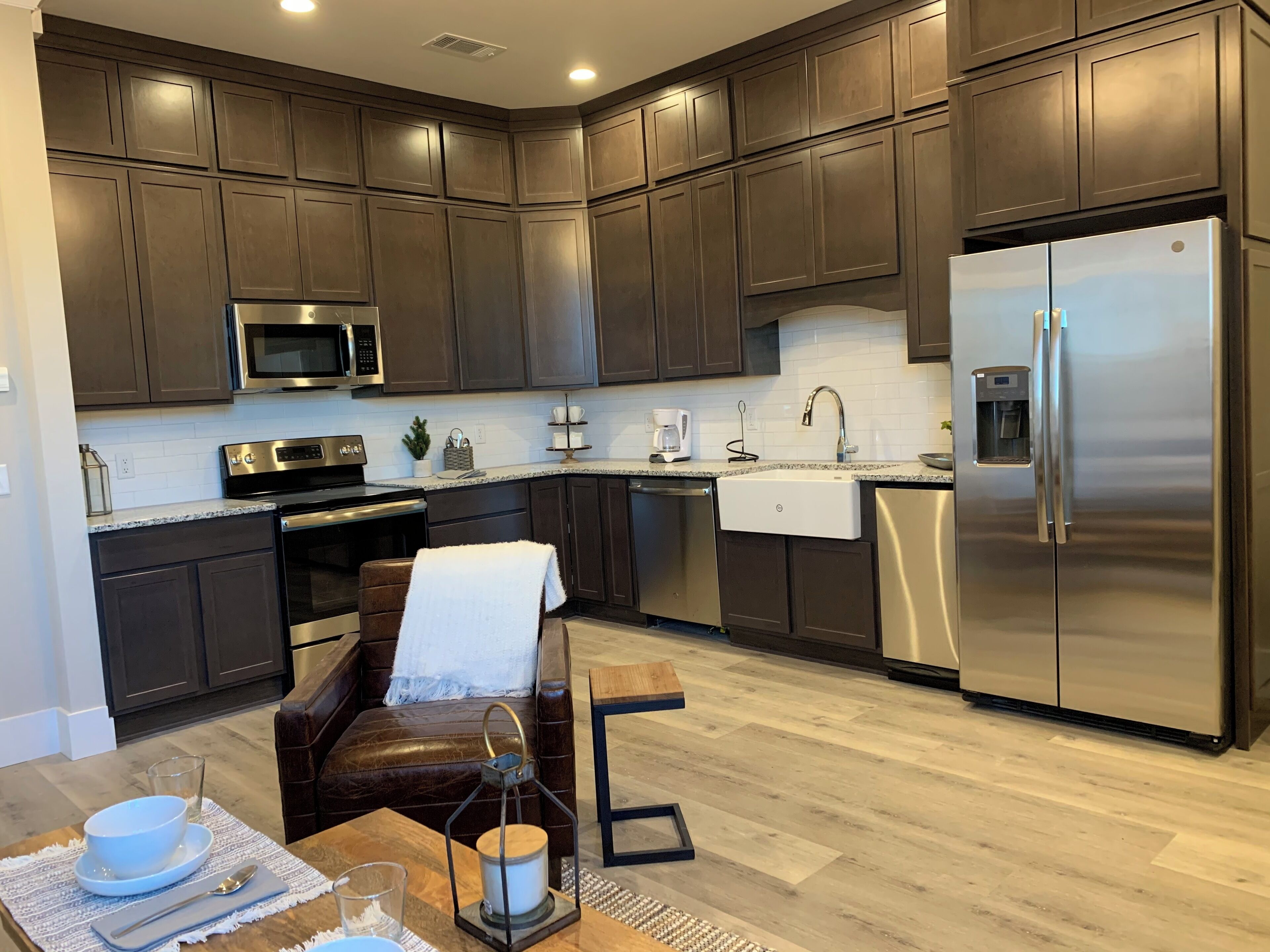 A modern kitchen with dark wood cabinets, stainless steel appliances, and a wooden dining table with a bench.