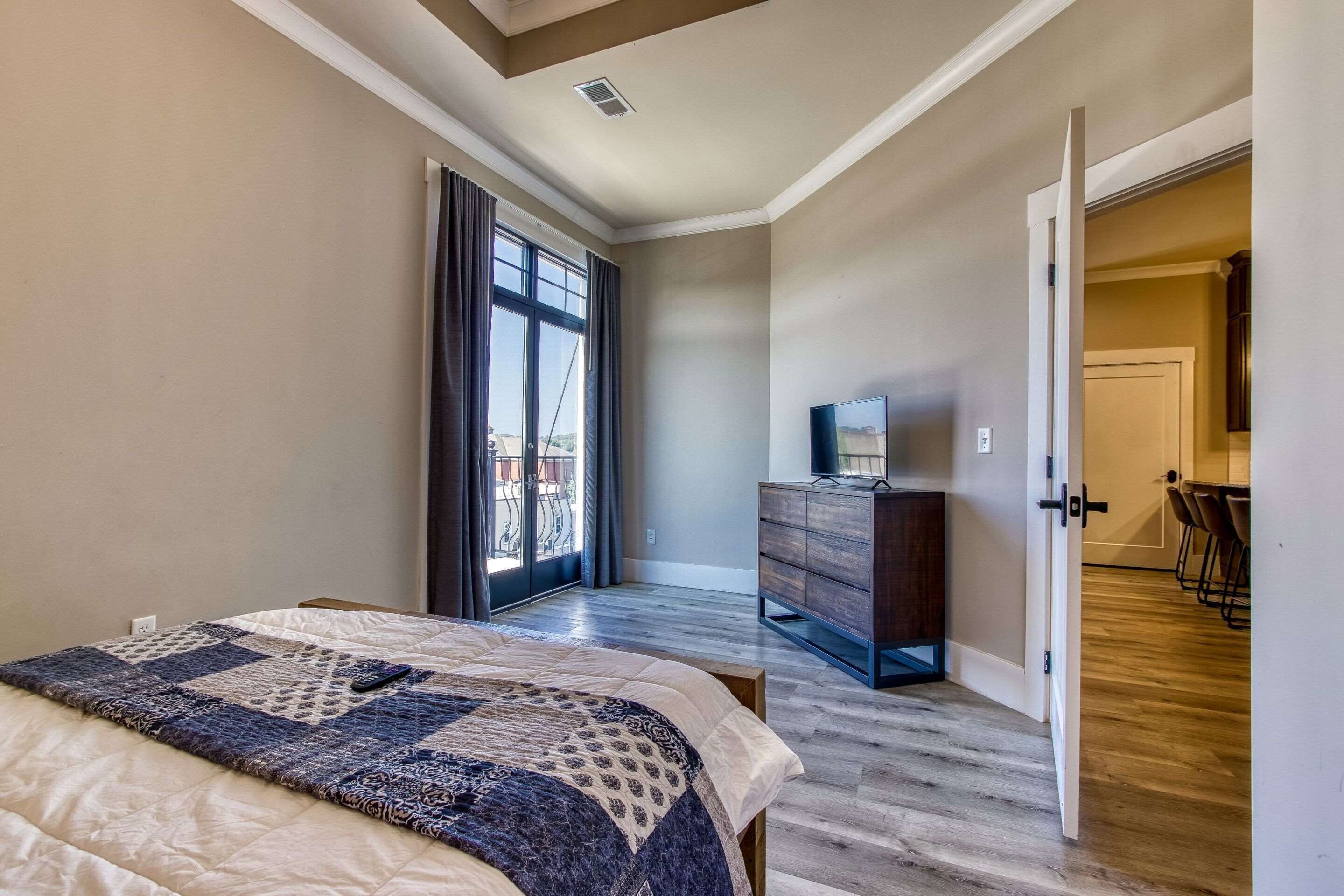 A bedroom with a large bed, a dresser, and a TV. There is a sliding glass door leading to a balcony.