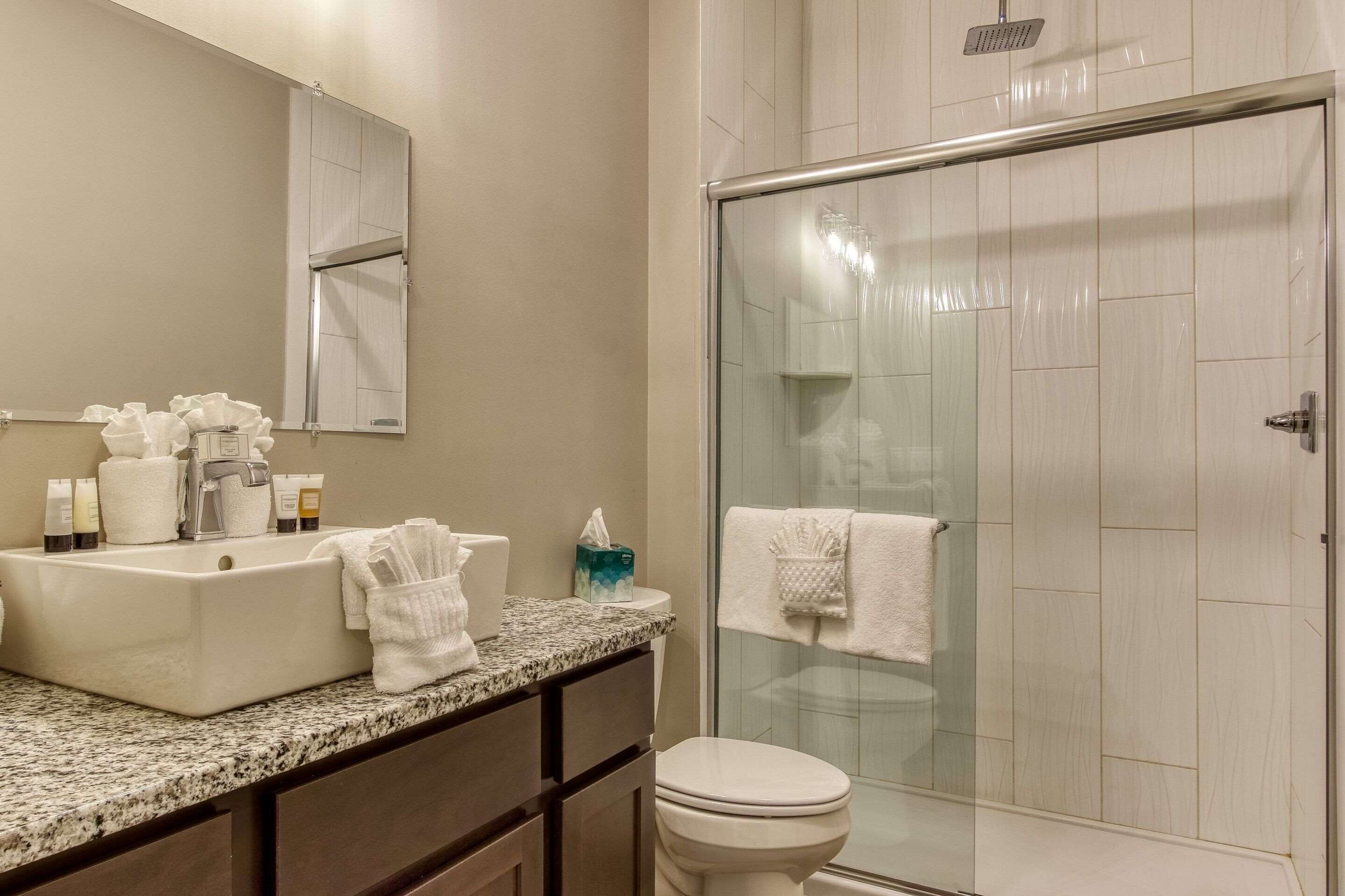 A modern bathroom with a glass-enclosed shower, a large sink with toiletries, and a toilet.