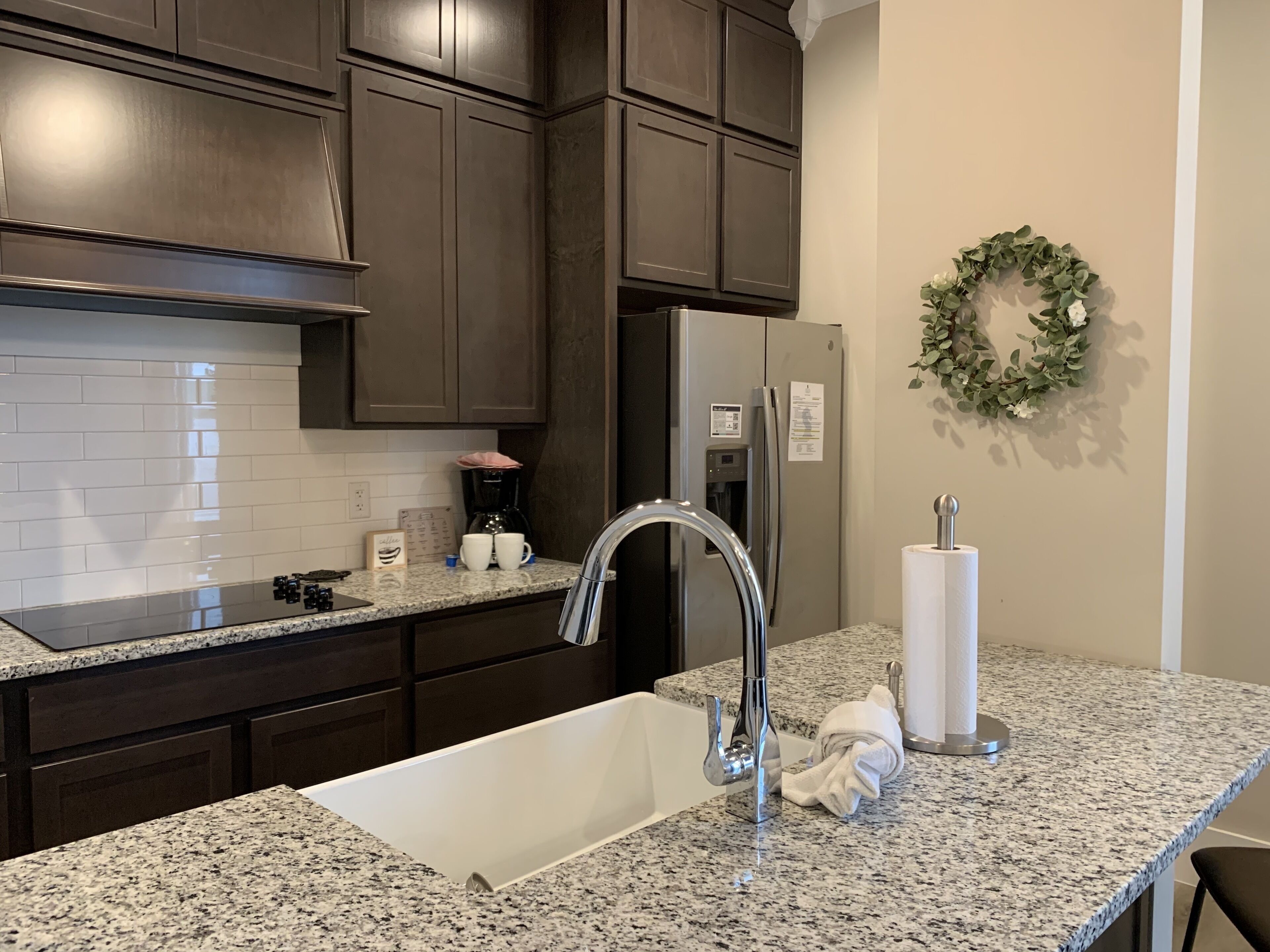 A kitchen with dark cabinets, a stainless steel refrigerator, a granite countertop, a sink, and a paper towel holder.