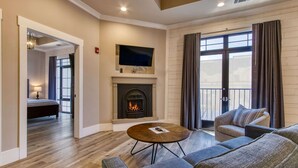 Una sala de estar con chimenea, un televisor montado encima y un balcón con cortinas.