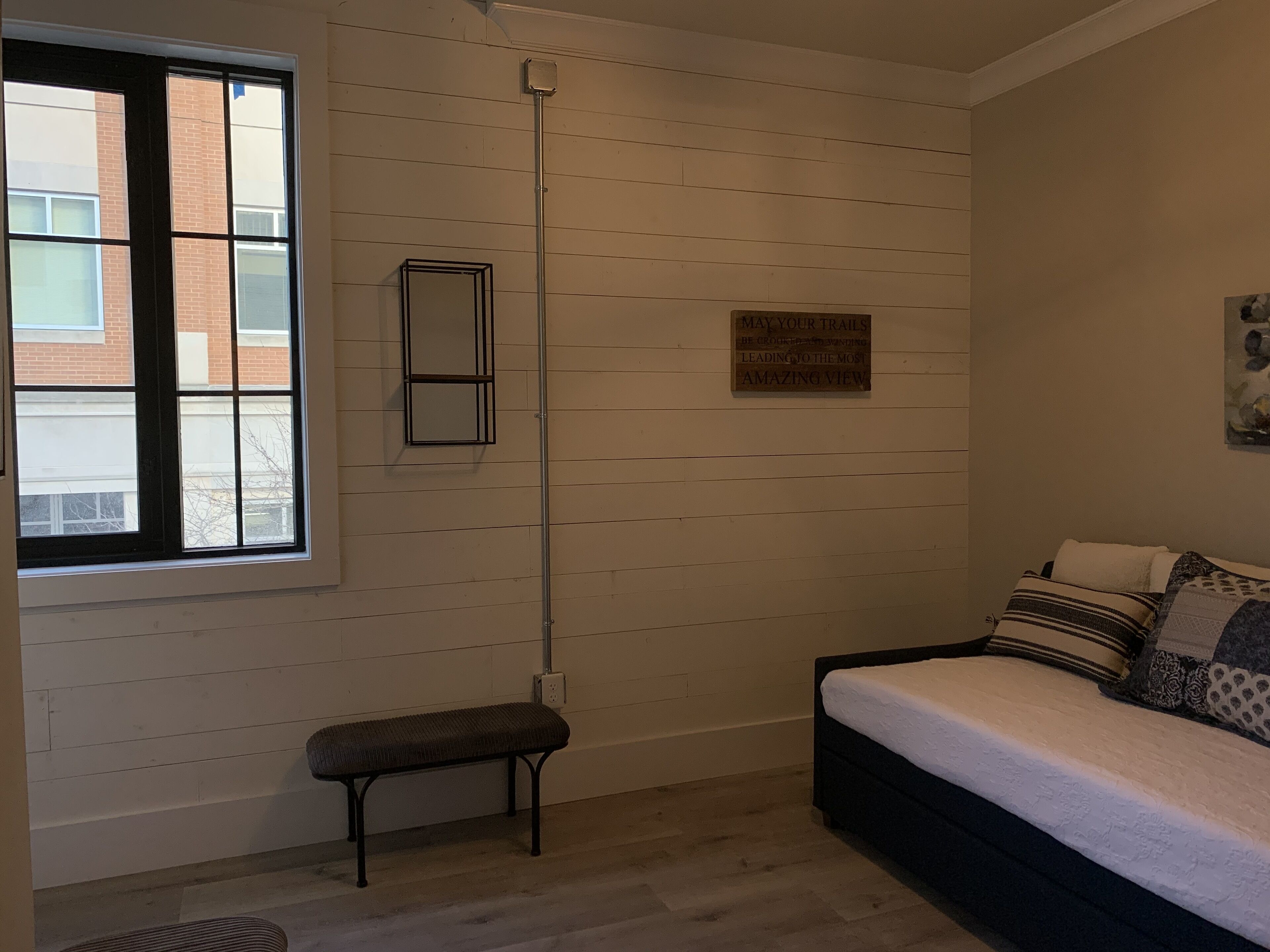 A room with a bed, bench, and a wall-mounted shelf.