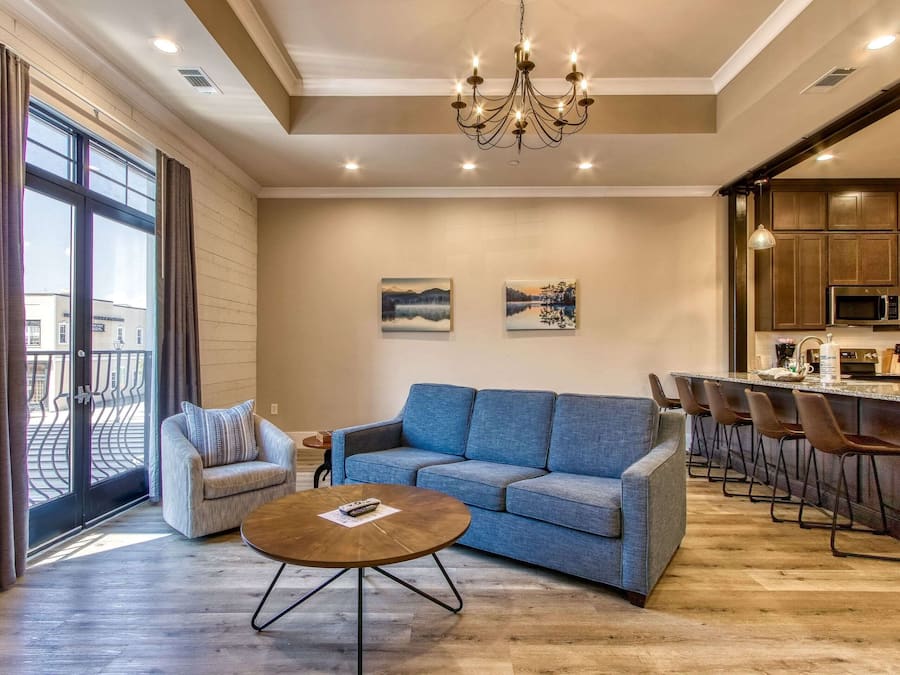 A modern living room with a sofa, a coffee table, and a kitchen area with bar stools.