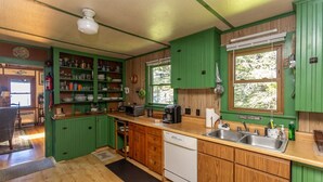 Une cuisine avec des meubles de rangement verts, des plans de travail en bois, un lave-vaisselle et une fenêtre donnant sur les arbres.