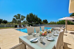 A poolside dining area with wicker furniture, a table set for two, and a view of the pool and surrounding greenery. - Villa 35 - Poseidon in Kouklia (Kouklia)