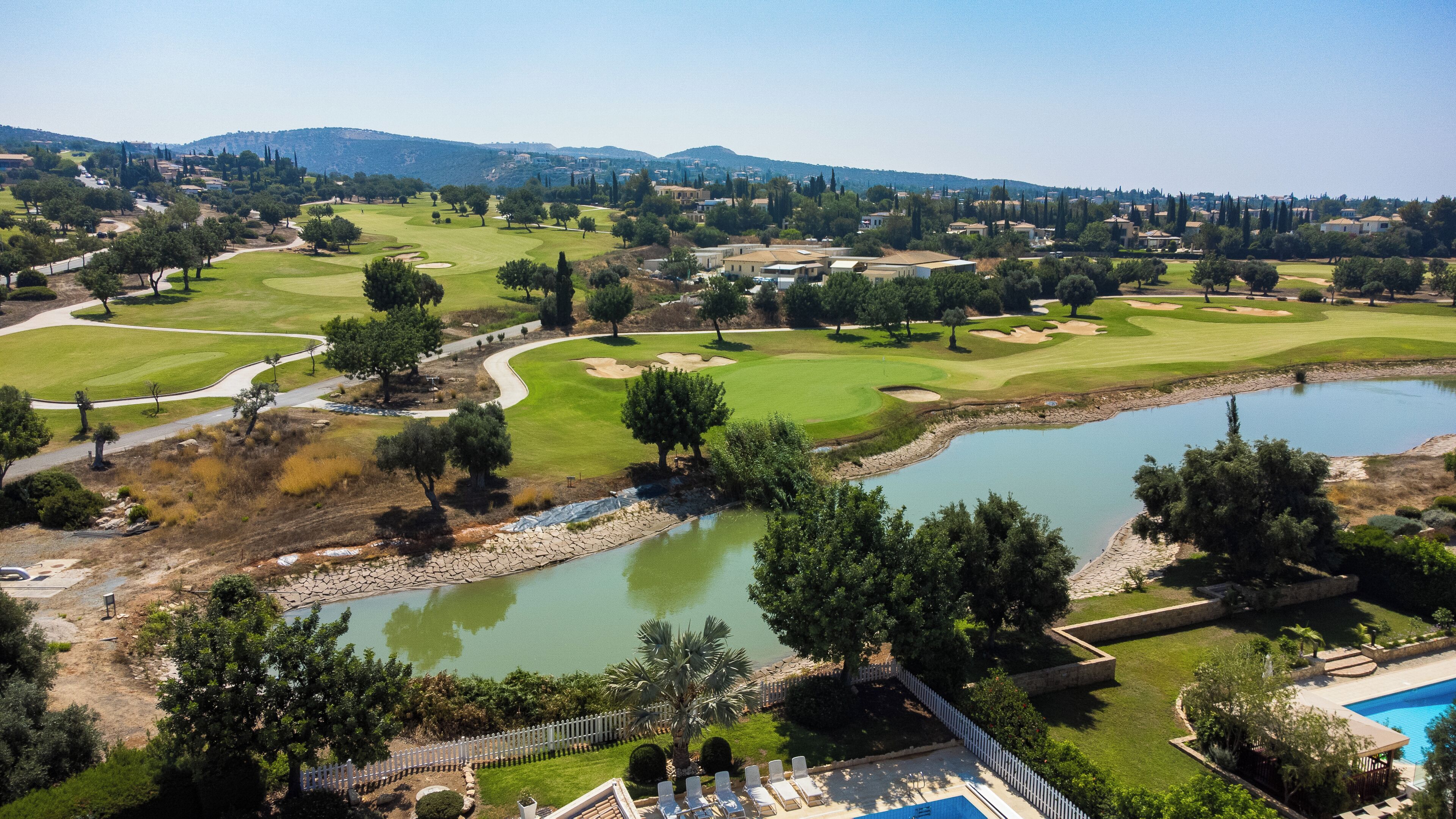 A golf course with a pond, trees, and a pool area.