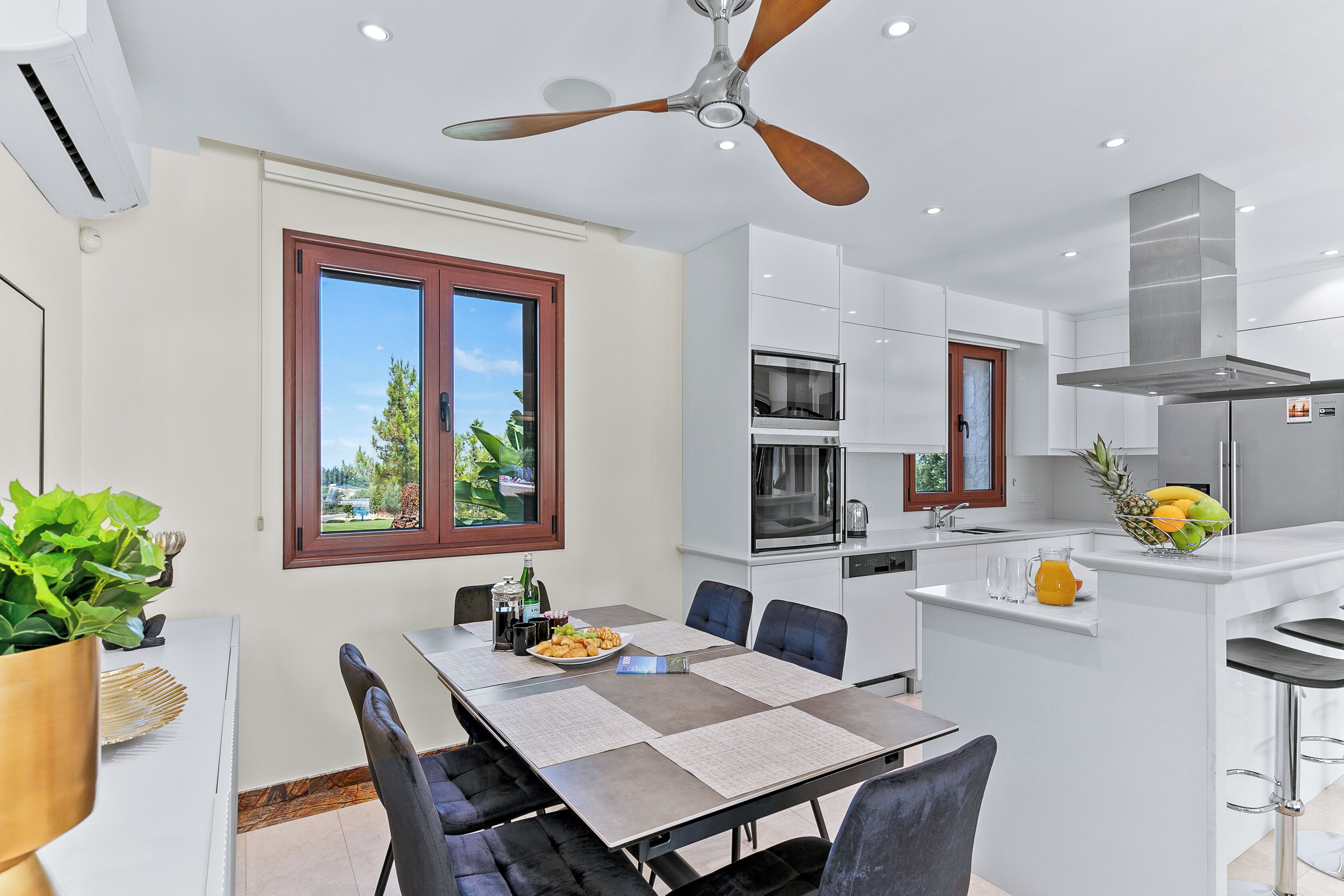 A modern kitchen with a dining area, featuring a large island, built-in appliances, and a ceiling fan.