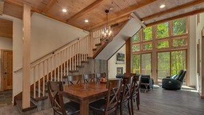 Un'ampia sala da pranzo con tavolo e sedie in legno, una scala con ringhiere in legno e ampie finestre che offrono vista sull'esterno.