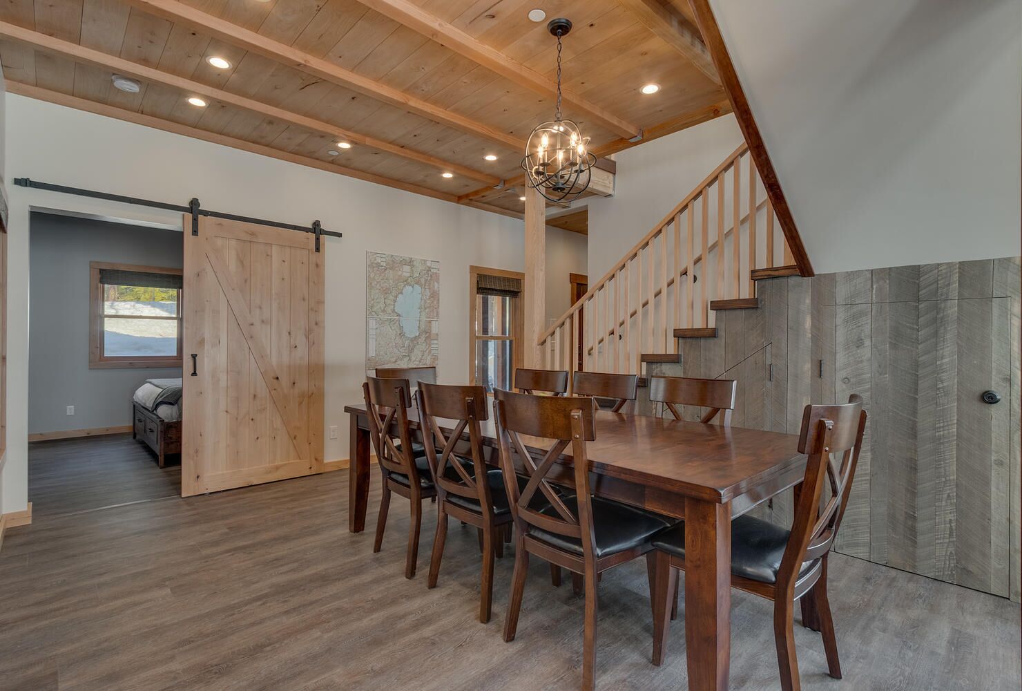 A spacious dining area with a wooden table and chairs, a chandelier, and a staircase with wooden railings.