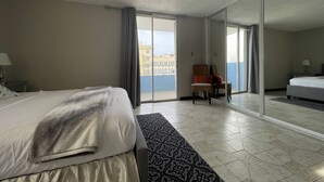 Een hotelkamer met een bed, een stoel, een kleine tafel en een grote spiegel die het balkon weerspiegelt.