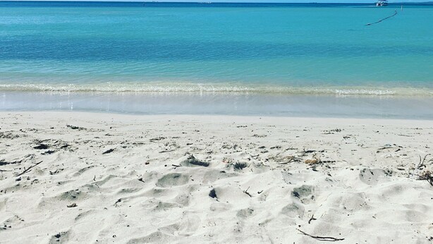 Een strand met helder turquoise water en een boot in de verte.