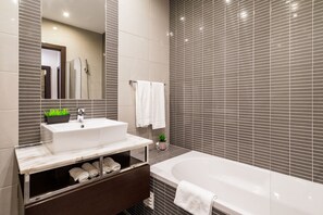A modern bathroom with a large bathtub, a sink with a mirror, and a vanity with a plant.