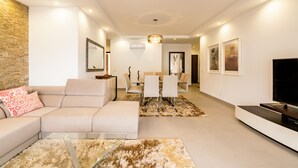 A modern living room with a sofa, a coffee table, a TV, and a dining area with chairs and a table.