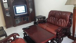 A living room with a dark wooden entertainment unit, a leather sofa, a matching armchair, and a small table. - Furnished apartment in Essaouira (Essaouira)