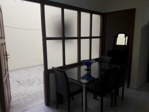 A room with a glass table and four chairs, a blue decorative item on the table, and a large window with frosted glass panels.