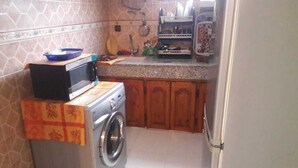 A compact kitchen with a washing machine, microwave, and wooden cabinets. - Furnished apartment in Essaouira (Essaouira)