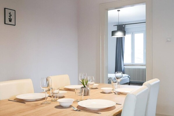 A dining area with a wooden table set for six, white chairs, and a modern pendant light. - Central 2 Bedroom Apartment 84 sq m with Private Parking (Novi Sad)