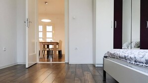 Un dormitorio con cama, armario y zona de comedor visible a través de una puerta abierta.